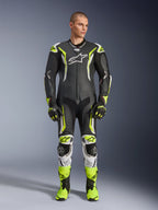 Alpinestars GP Tech V5 skinnställ, professionell motorcykelracingoverall i svart och neongul fluo med vita detaljer, bärs av en modell med matchande racinghandskar och stövlar, med aerodynamisk design och skyddande sliders.