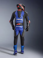 Alpinestars Yamaha GP-R7 läderdräkt i ett stycke, baksida av en motorcykelförare i full racingutrustning, metallicblå och svart med vita och röda detaljer, med Yamaha- och GYTR-logotyper på den aerodynamiska puckeln, bärs med matchande blå stövlar och en racinghjälm.