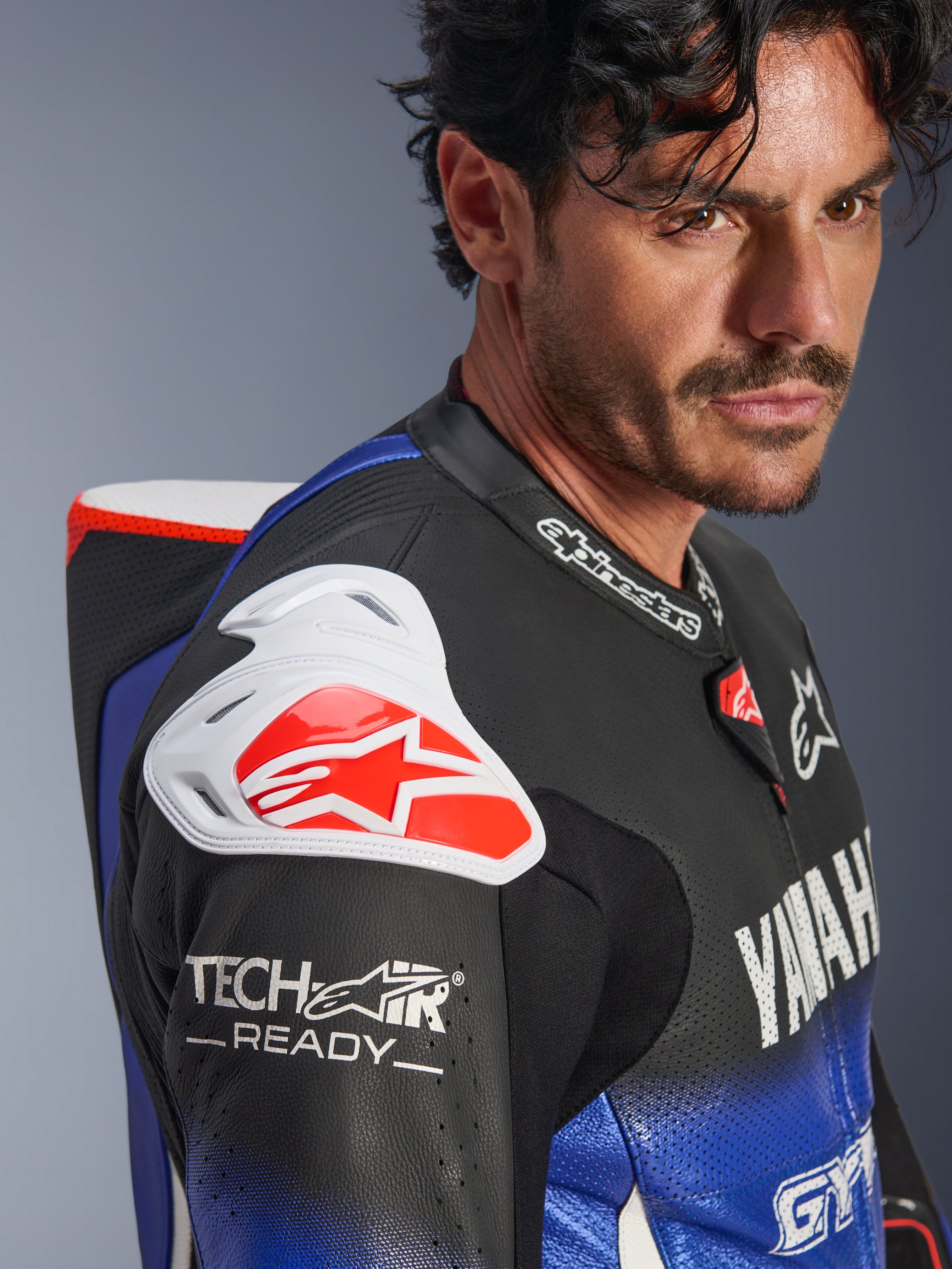 Yamaha GP-R7 endelad läderdräkt, metallicblå, svart, vit och röd, närbild av axel och bröst, vitt DFS-axelskydd med röd logotyp, aerodynamisk puckel, Tech-Air Ready-märkning på den perforerade läderärmen.