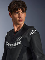 Close-up of a man wearing the Alpinestars GP Force V2 Leather Suit in Black, featuring perforated leather construction, Alpinestars logo with 'RACING AHEAD' branding on the chest, and white star logo on the shoulder sliders.