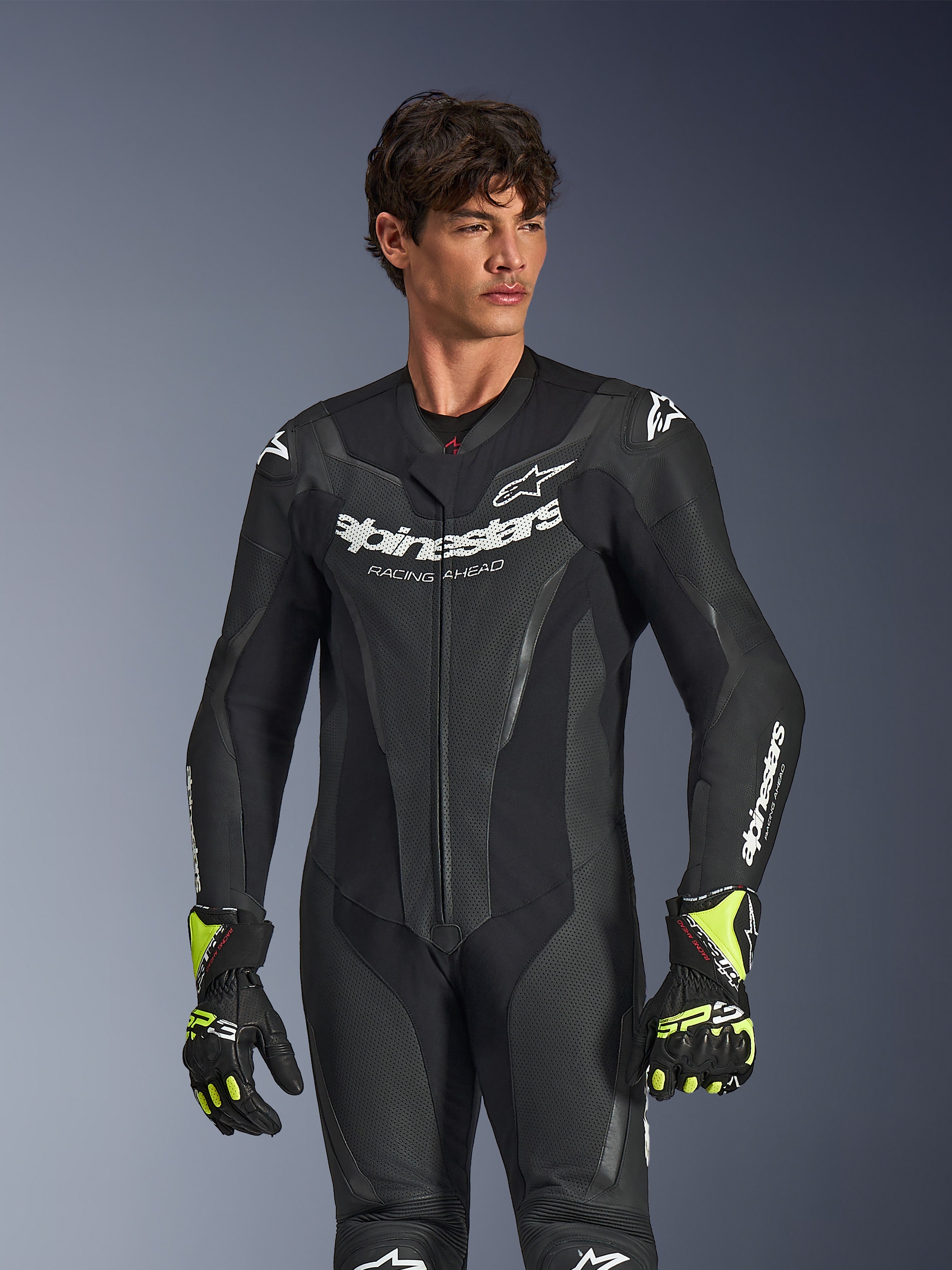 Alpinestars GP Force V2 Leather Suit 1-Piece, Black, white Alpinestars branding and logo, perforated leather panels for ventilation, worn by a male model with black and neon yellow gloves, high-performance motorcycle racing gear