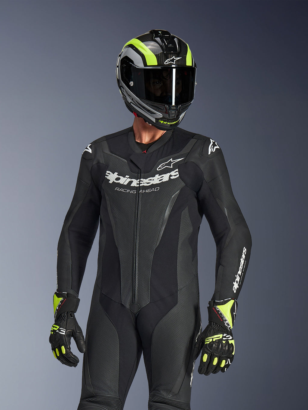 Alpinestars GP Force V2 Leather Suit 1-Piece, Black, worn by a rider with a black and neon yellow helmet and gloves, featuring white Alpinestars branding on the chest, perforated leather panels for ventilation, and a professional race-ready design.