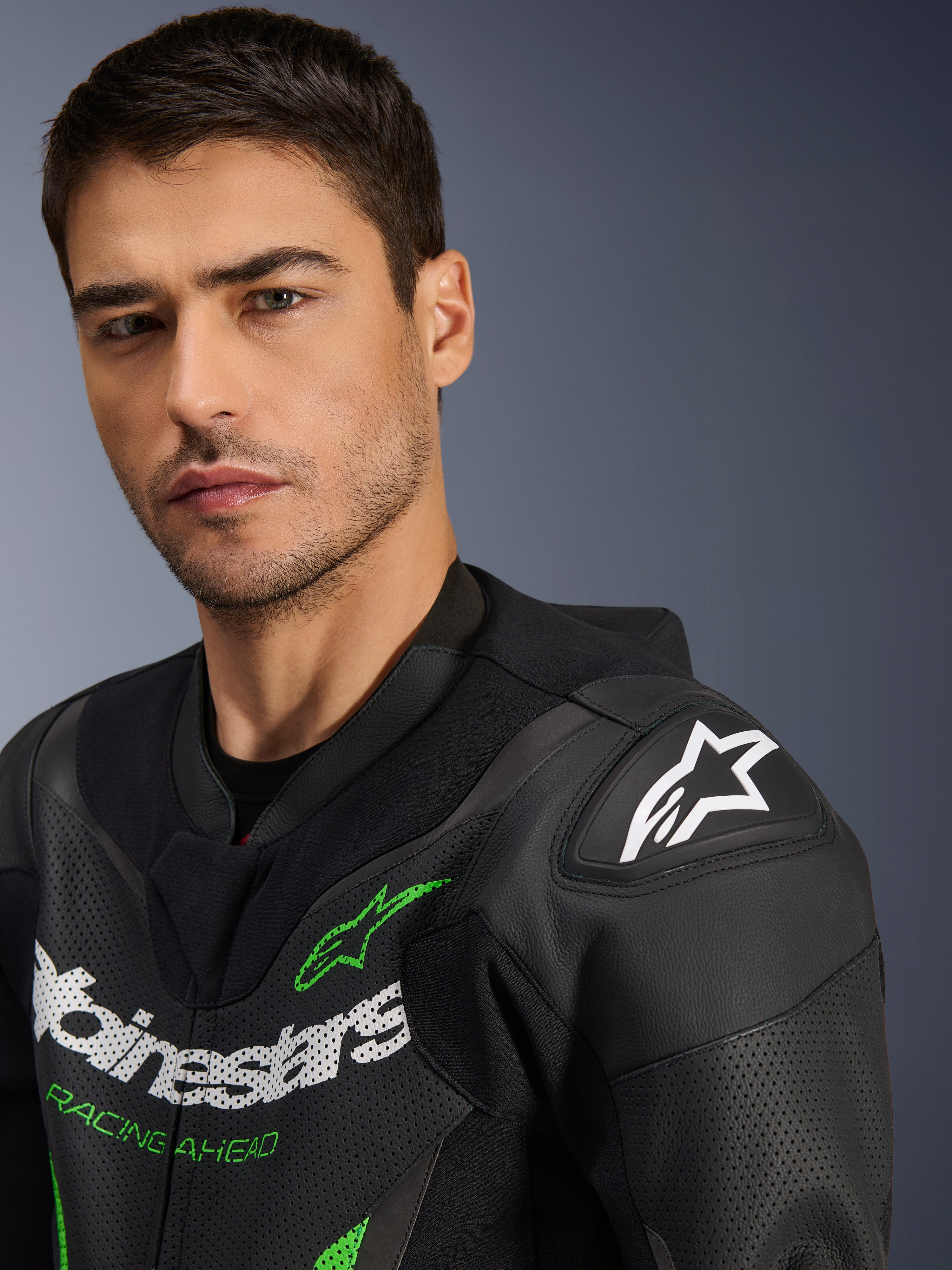 Alpinestars GP Force V2 skinnställ – 1-delat, svart och grönt, närbild av en manlig modell som bär racingstället, med vit och grön logotyp, perforerade läderpaneler och DFS Lite-axelskydd med en vit stjärnlogotyp.