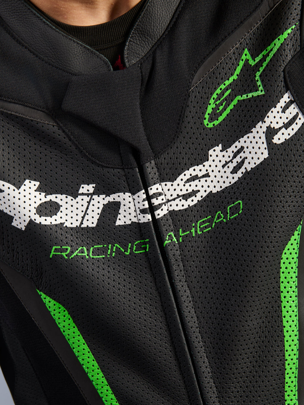 Alpinestars GP Force V2 Leather Suit - 1Piece, närbild på bröstpartiet, svart perforerat läder med vit Alpinestars-branding, grön 'RACING AHEAD'-text och gröna detaljer