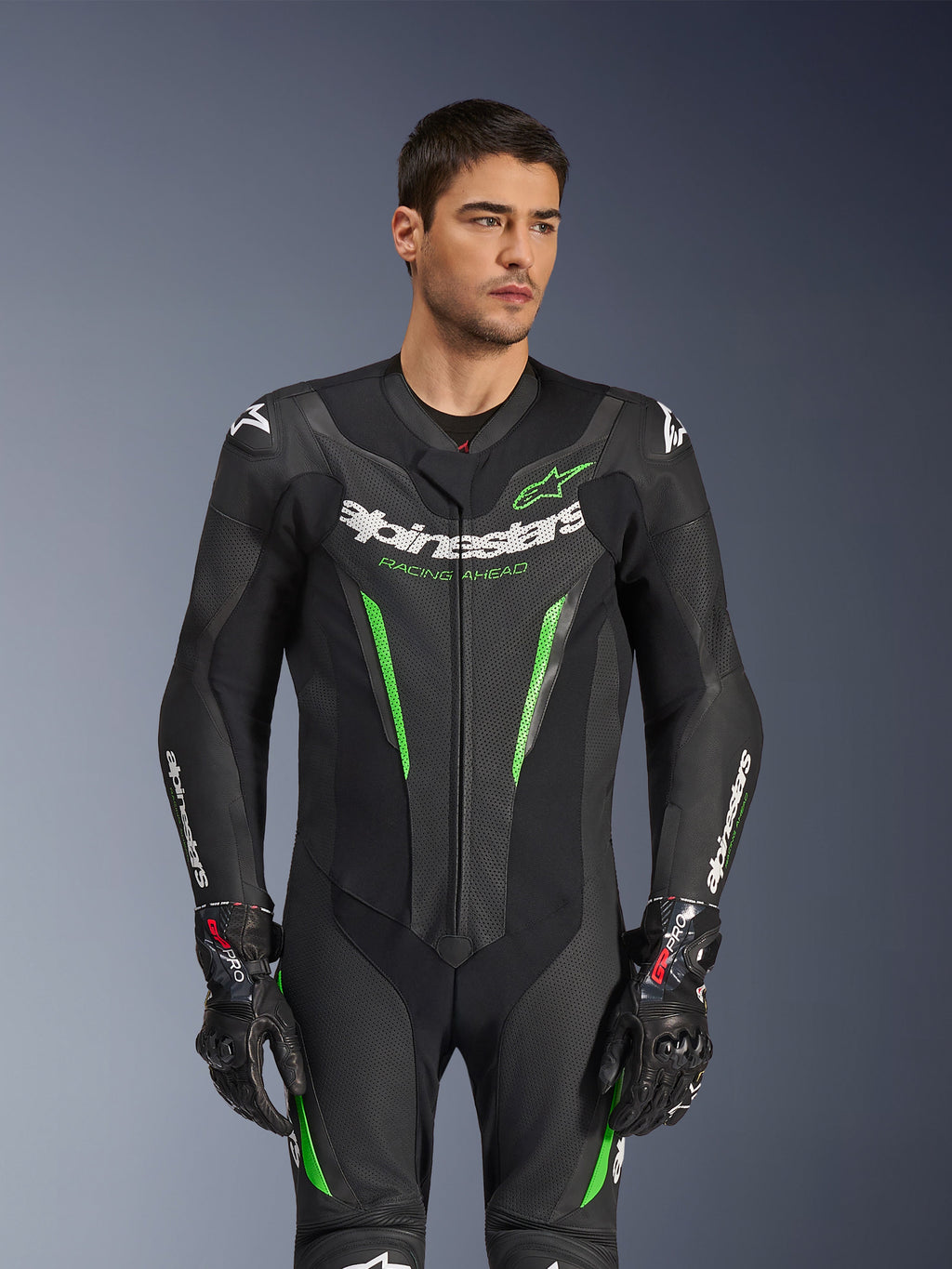 Alpinestars GP Force V2 Skinnställ - 1 del, svart och grönt racingskinnställ för motorcykel, bärs av modell, med perforerade läderpaneler, tydlig vit Alpinestars-logotyp på bröstet och ärmarna, samt integrerat axelskydd för banprestanda