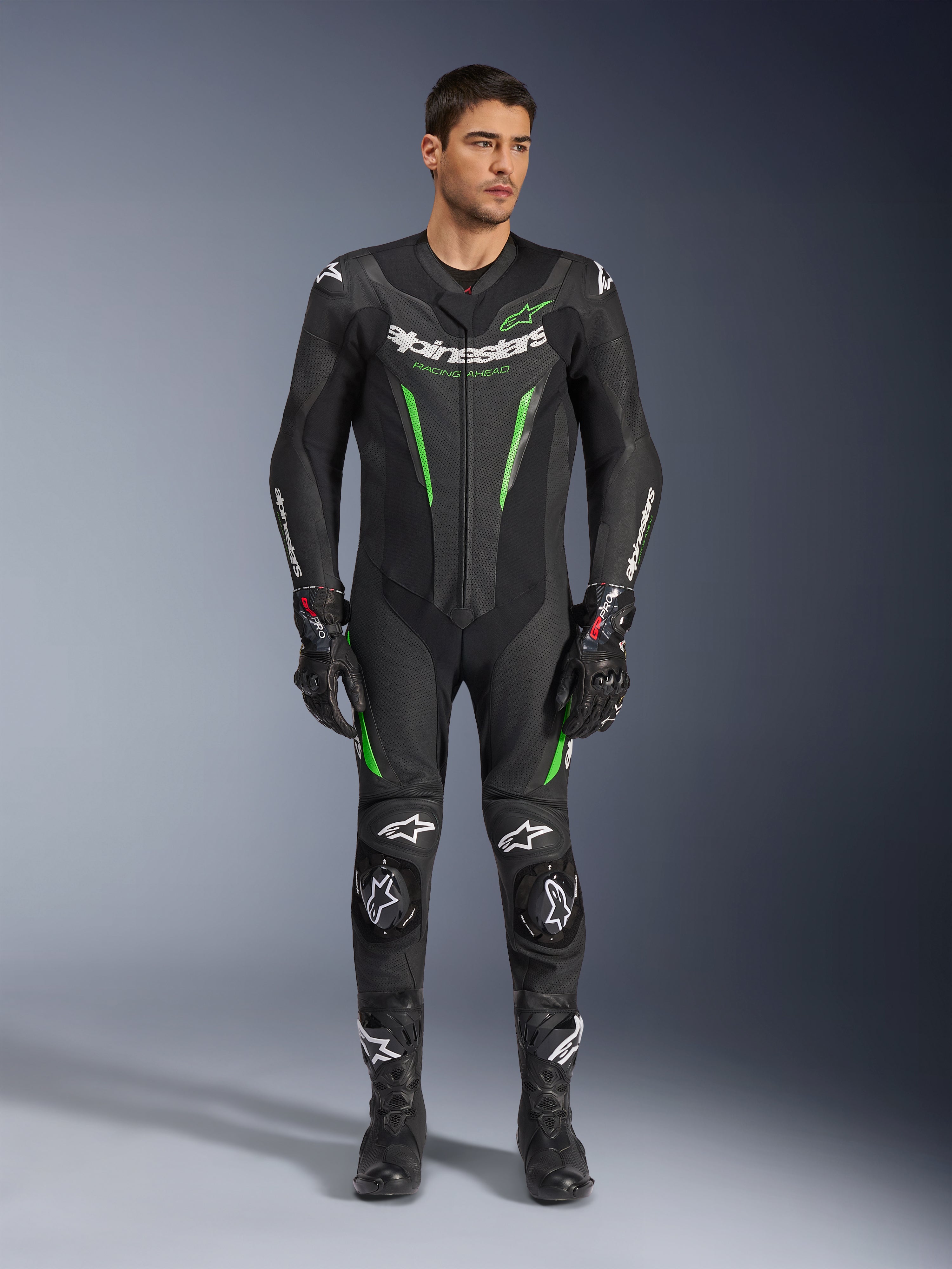 Alpinestars GP Force V2 Leather Suit - 1Piece, heldelat skinnställ för motorcykelracing, svart och grön, frontvy av en modell i stället med vit logotyp på bröstet och neongröna detaljer, med perforerat läder och externa axelskydd, kombinerat med svarta racinghandskar och stövlar