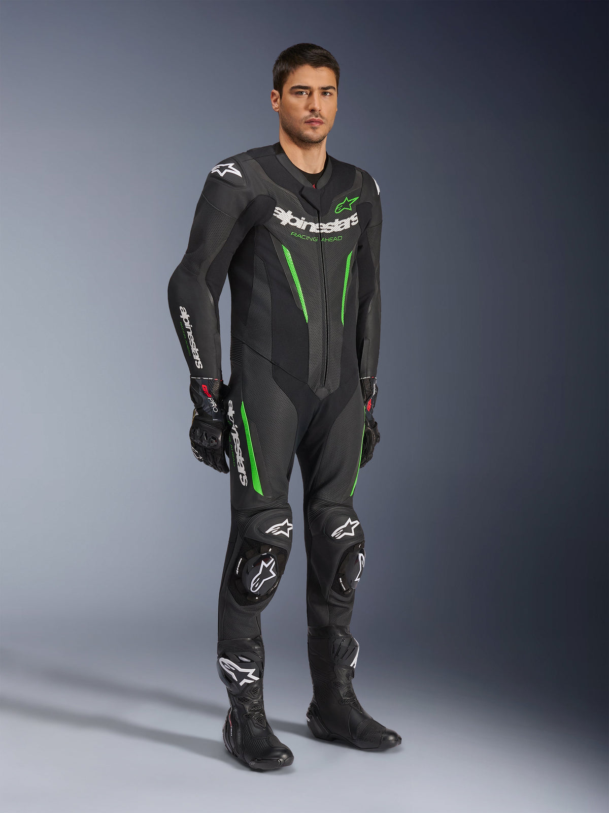 Alpinestars GP Force V2 skinnställ i ett stycke, svart och grönt, komplett racingutrustning buren med svarta handskar och stövlar, med perforerade läderpaneler, vit Alpinestars-logotyp och integrerade knäpuckar, professionellt tävlingsställ för bana