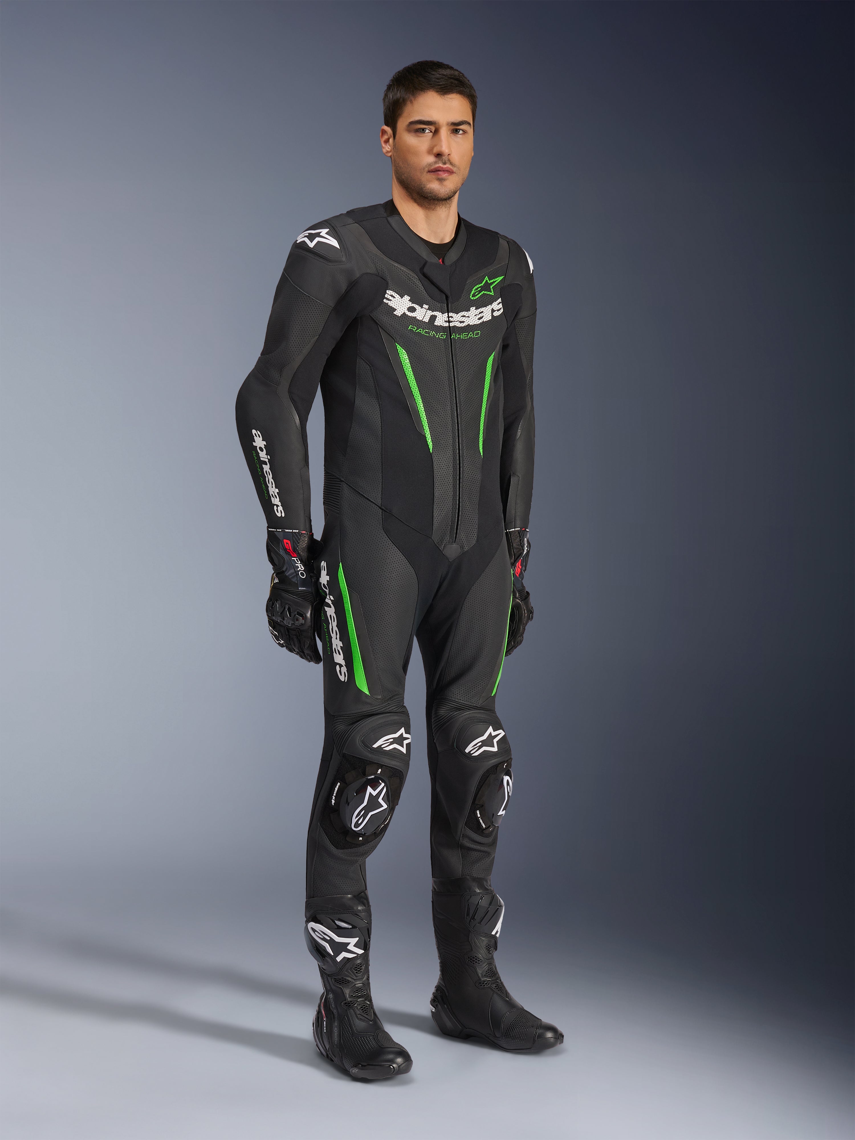 Alpinestars GP Force V2 skinnställ i ett stycke, svart och grönt, komplett racingutrustning buren med svarta handskar och stövlar, med perforerade läderpaneler, vit Alpinestars-logotyp och integrerade knäpuckar, professionellt tävlingsställ för bana