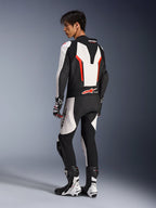 Motorcykelförare i Alpinestars GP Force V2 Leather Suit - 1Piece i vitt, svart och rött fluo, vy från sidan och bakifrån som visar den aerodynamiska puckeln och perforerade läderpaneler, matchat med racingstövlar och handskar för bana- och prestandakörning.