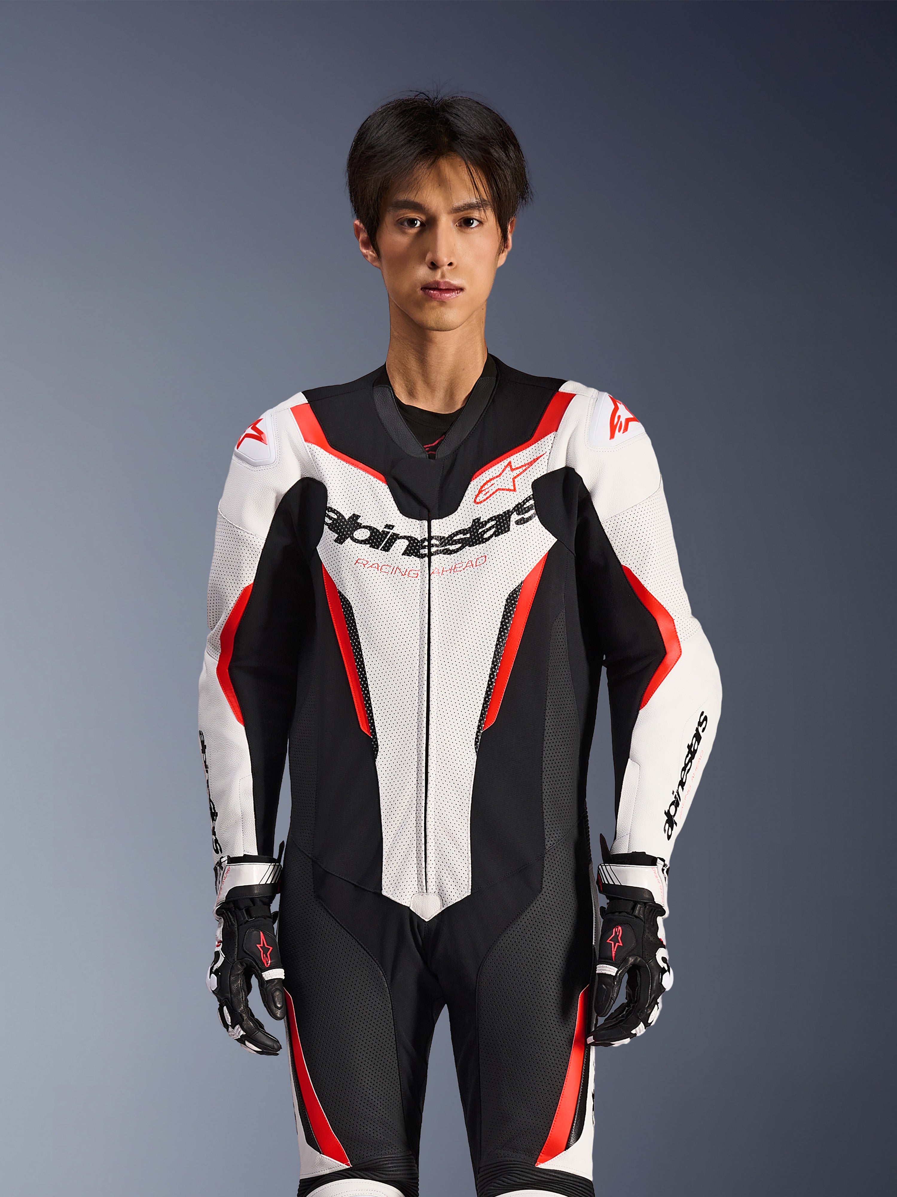 Alpinestars GP Force V2 läderställ - 1 del, vit, svart och röd fluo, bärs av en manlig modell, med perforerade läderpaneler och tydlig Alpinestars-logotyp på bröstet, kombinerat med svarta och vita racinghandskar, designat för bana- och prestandakörning