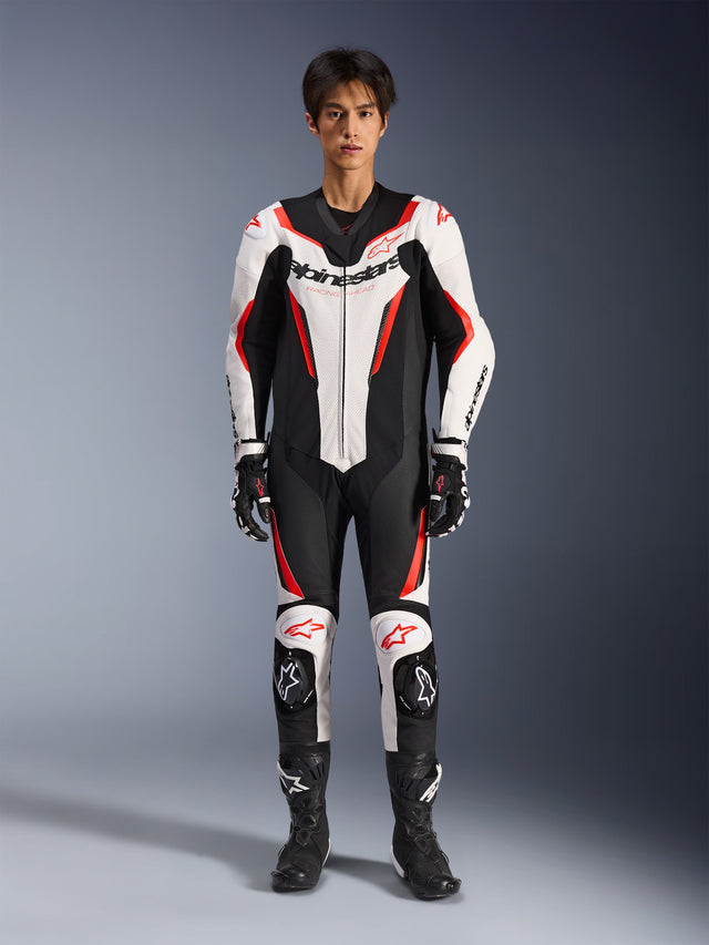 Alpinestars GP Force V2 skinnställ - helställ, vit svart röd fluo, helställ i läder för racing, frontvy på modell, med perforerade paneler och röda accenter, tydlig Alpinestars-logotyp på bröstet, stylad med professionella racingstövlar och handskar