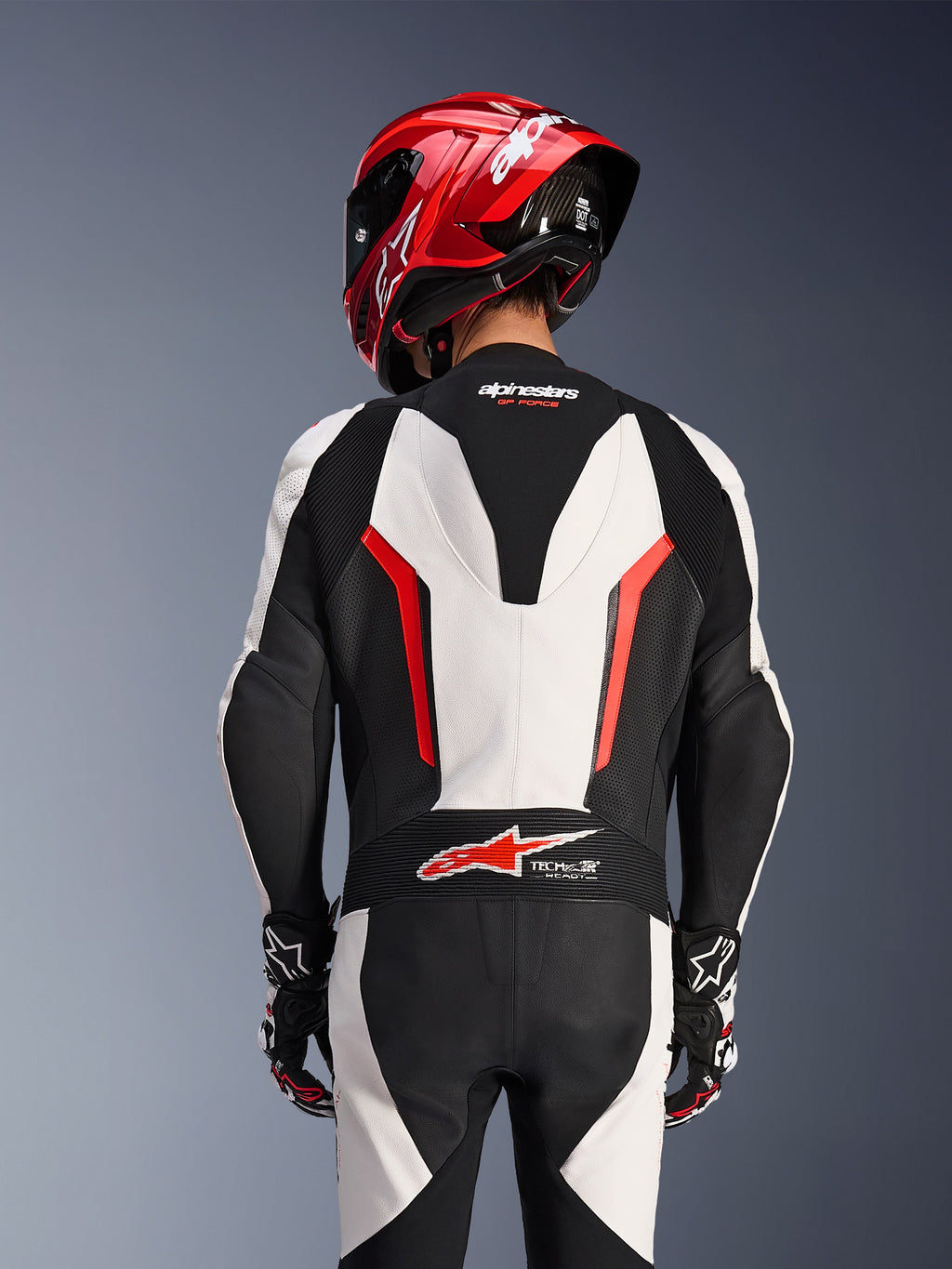 Vy bakifrån av Alpinestars GP Force V2 1-Piece läderställ i vitt, svart och röd fluo, buren med en röd racinghjälm, med Tech-Air Ready-märkning på nedre ryggen, perforerade läderpaneler och dragspelspaneler för racingprestanda.