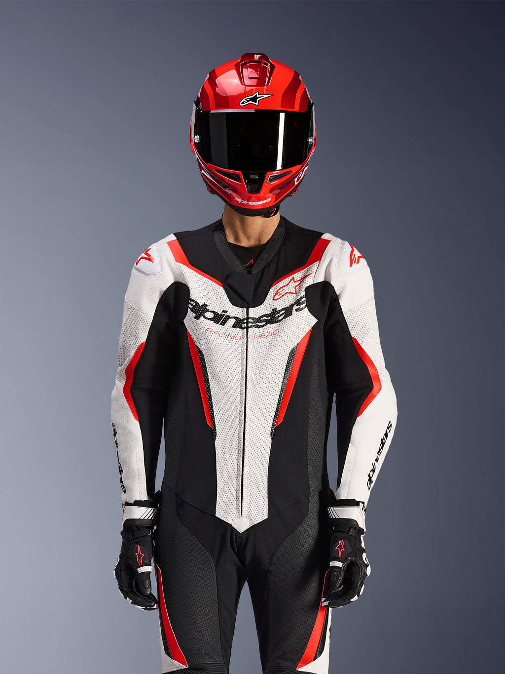 Alpinestars GP Force V2 skinnställ - 1 del, vit, svart och röd fluo, bärs med röd integralhjälm och svarta racinghandskar, perforerade läderpaneler och framträdande Alpinestars-logotyp på bröstet, professionell racingutrustning för motorcykel