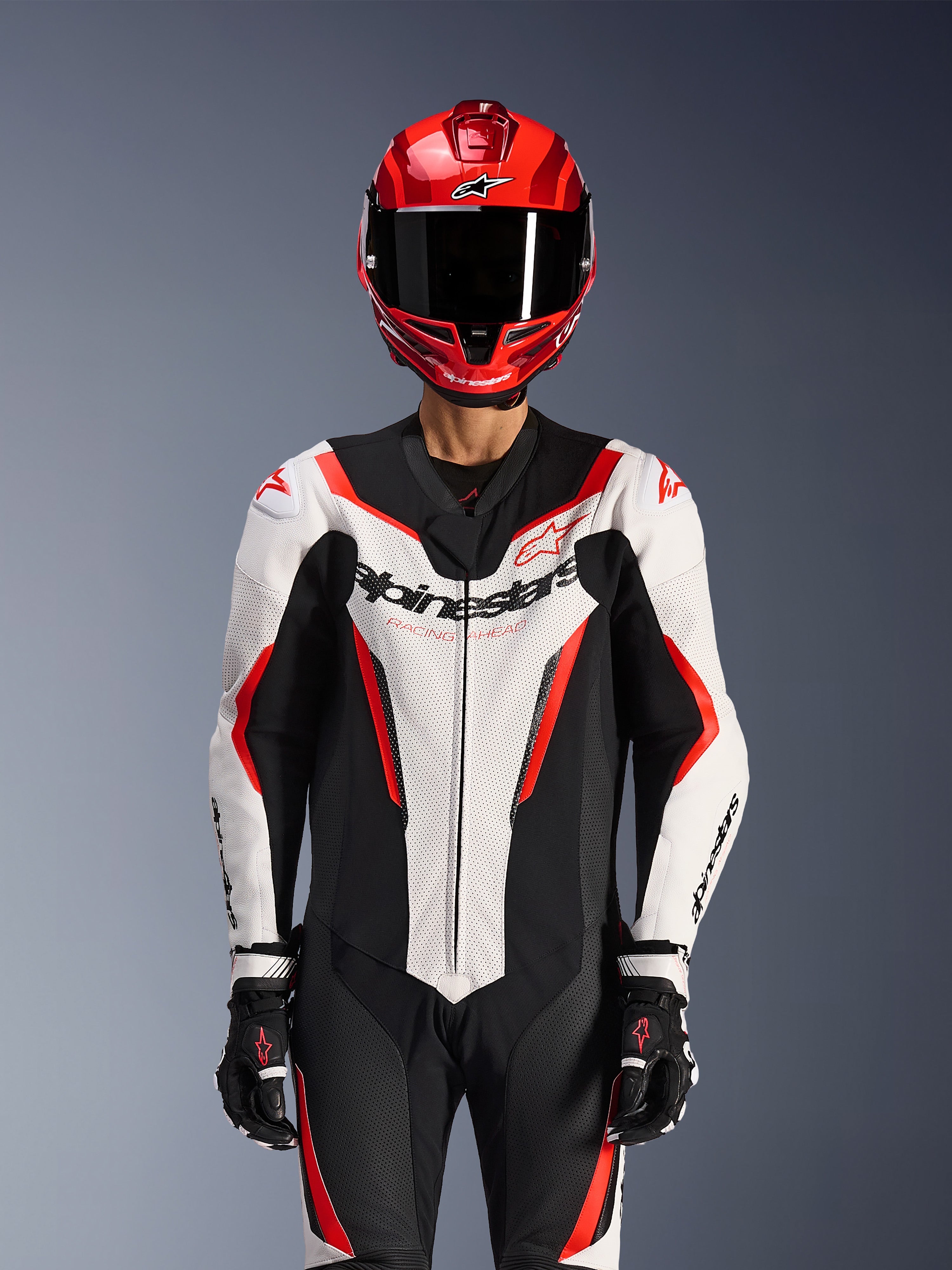 Alpinestars GP Force V2 skinnställ - 1 del, vit, svart och röd fluo, bärs med röd integralhjälm och svarta racinghandskar, perforerade läderpaneler och framträdande Alpinestars-logotyp på bröstet, professionell racingutrustning för motorcykel
