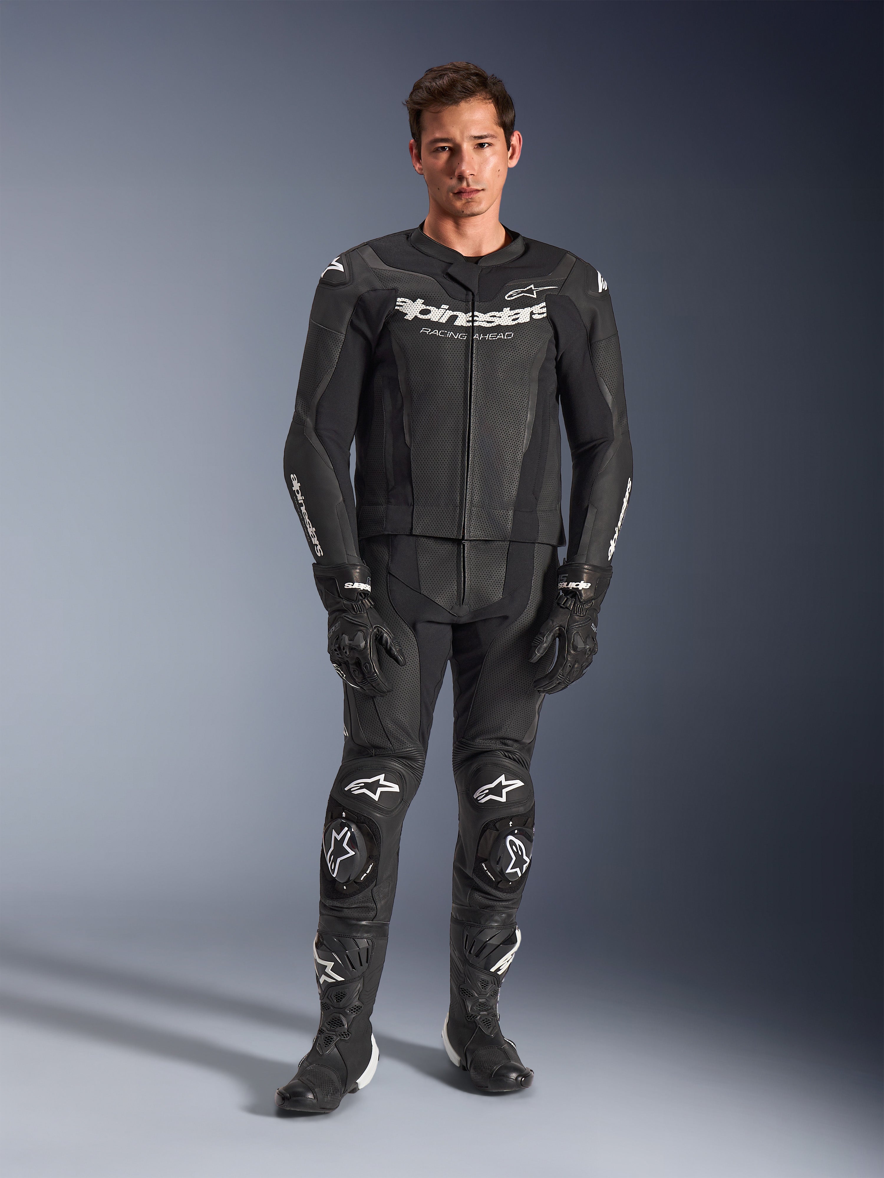 Alpinestars GP Force V2 Leather Suit 2-Piece, Black with white logos, full-body motorcycle racing suit, featuring premium leather construction with reinforced knee sliders and perforated panels, worn with black gloves and boots, studio full-length view
