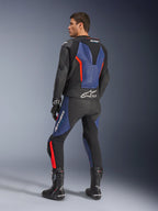 Alpinestars GP Force V2 läderställ i två delar, svart, blå och fluorescerande röd, profilvy bakifrån på en modell, med aerodynamisk puckel, perforerat läder och Tech-Air Ready-märkning, bärs med svarta Alpinestars racingstövlar och handskar