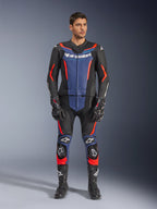 Alpinestars GP Force V2 Leather Suit 2-Piece i svart, blått och fluorescerande rött, med blå paneler på bröstet och underbenen samt livfulla röda fluorescerande detaljer, buren av en manlig modell med svarta racingstövlar och handskar, professionell skyddsutrustning för motorsport