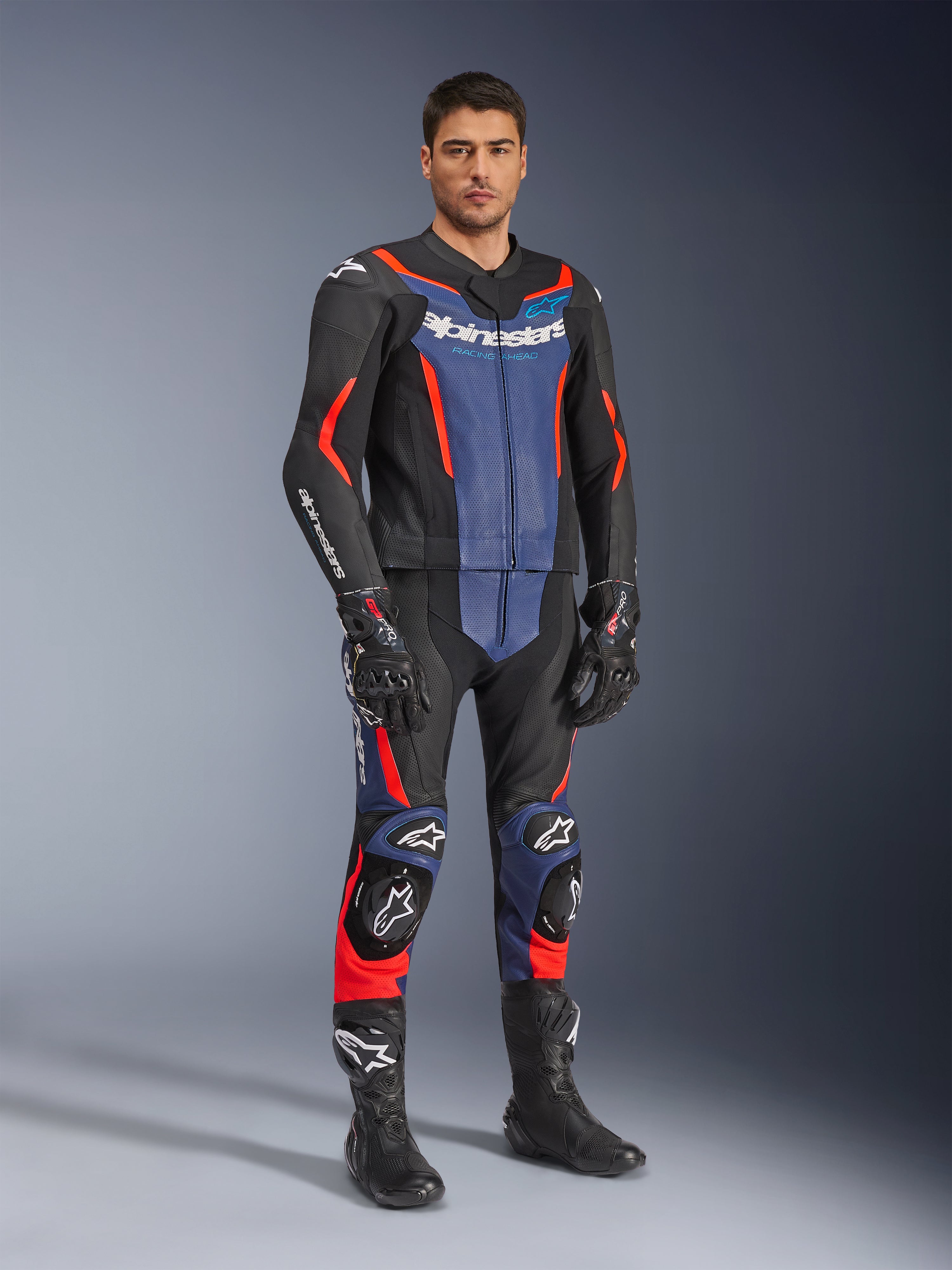 Alpinestars GP Force V2 tvådelat skinnställ, MC-ställ i läder, svart, blå och röd fluo, bärs med matchande svarta racinghandskar och stövlar, med perforerade paneler och skyddande sliders, aerodynamisk design för sportkörning