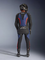 Alpinestars GP Force V2 Läderställ 2-delat, Black Blue Red Fluo, fullständig vy bakifrån av en förare i komplett racingutrustning, med blå läderpaneler på ryggen och benen med fluorescerande röda accenter, Tech-Air® Ready-logotyp på nedre ryggen, tillsammans med en kolfiberhjälm, svarta handskar och racingstövlar.
