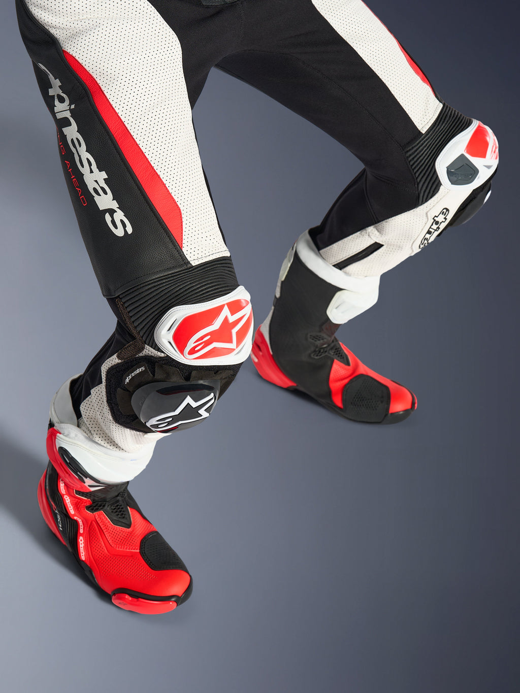 Alpinestars Stella GP-R7 2-delars läderställ för dam, underben och racingstövlar, svart, vit och röd fluo, med perforerat läder, framträdande Alpinestars-logotyp på låret, dragspelspaneler och röd-vita knäpuckar med matchande röd-svarta tekniska stövlar.
