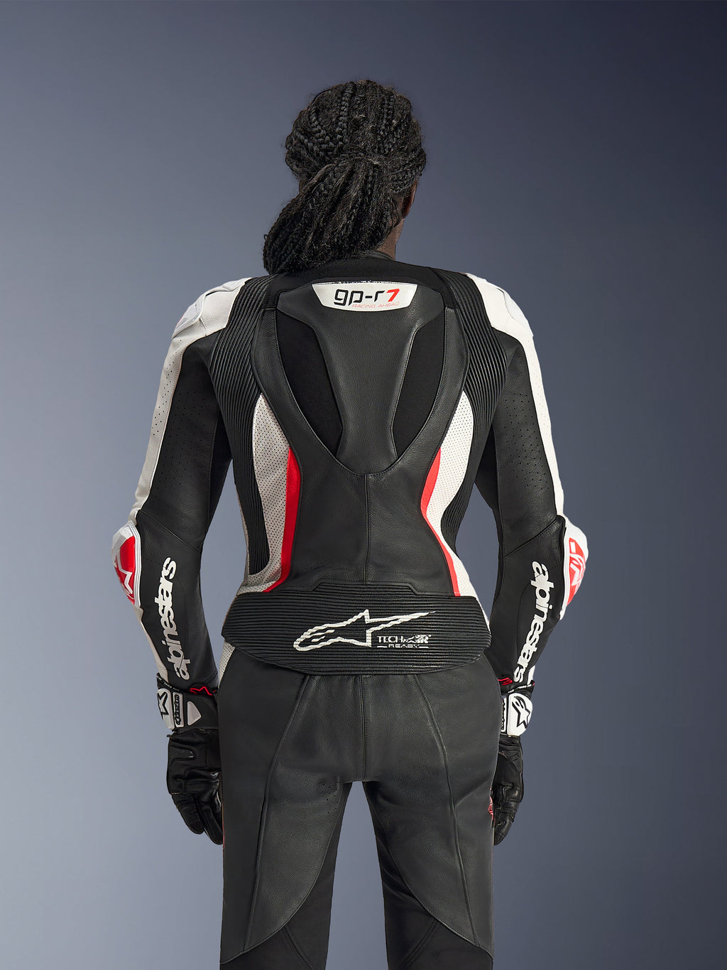 Vy bakifrån av Alpinestars Stella GP-R7 2-delat läderställ i svart, vitt och Red Fluo, med en aerodynamisk puckel med GP-R7-märkning, perforerade läderpaneler, dragspelspaneler och Tech-Air® Ready-logotyp på nedre delen av ryggen.