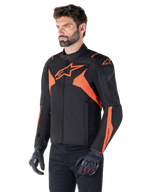 Alpinestars T-Jaws V4 Waterproof Jacket, svart och röd fluo, sportmotorcykeljacka buren av en manlig modell, med framträdande orangea stjärnlogotyper på bröstet och axlarna, matchad med svarta handskar och byxor