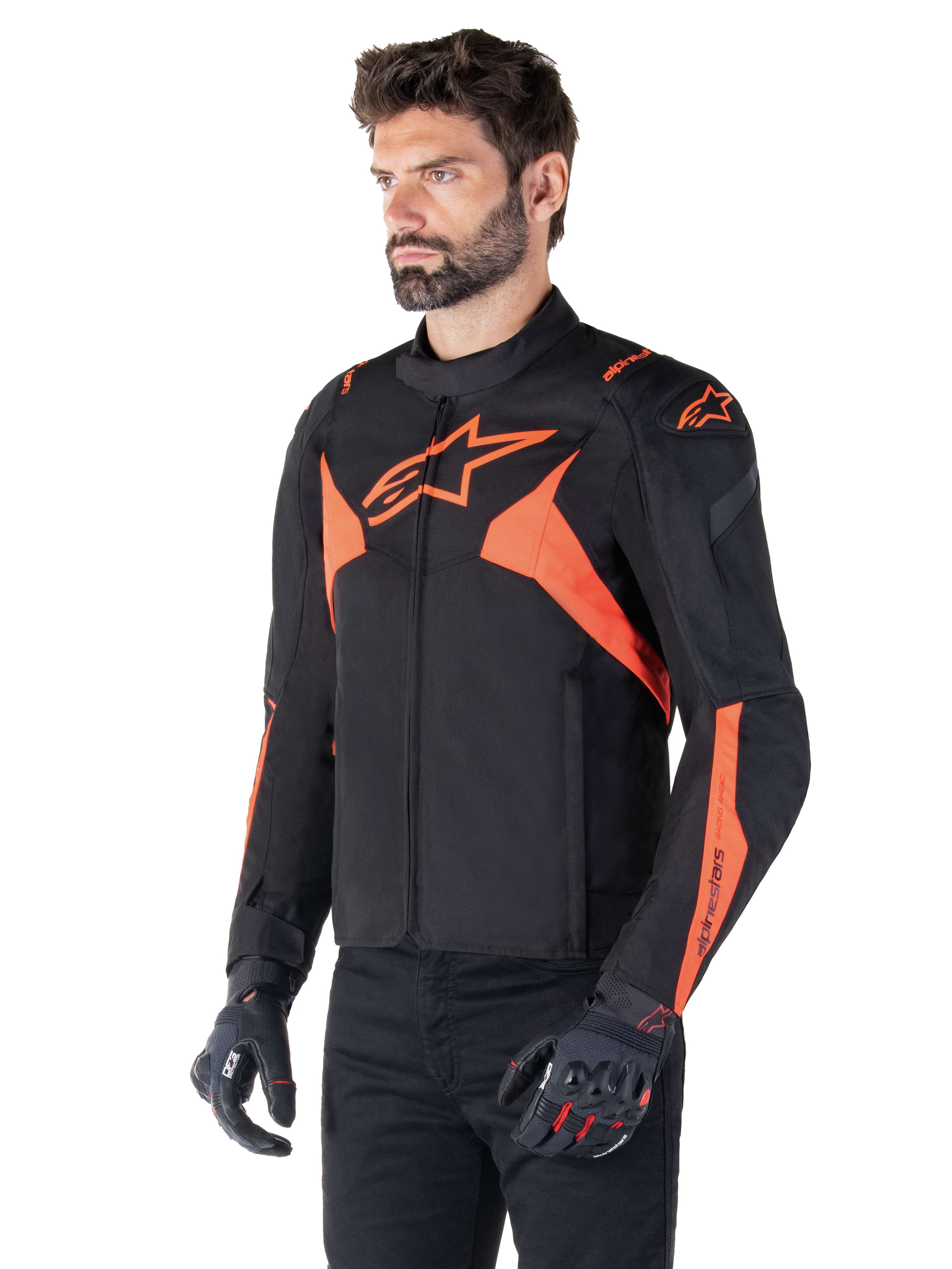Alpinestars T-Jaws V4 Waterproof Jacket, svart och röd fluo, sportmotorcykeljacka buren av en manlig modell, med framträdande orangea stjärnlogotyper på bröstet och axlarna, matchad med svarta handskar och byxor
