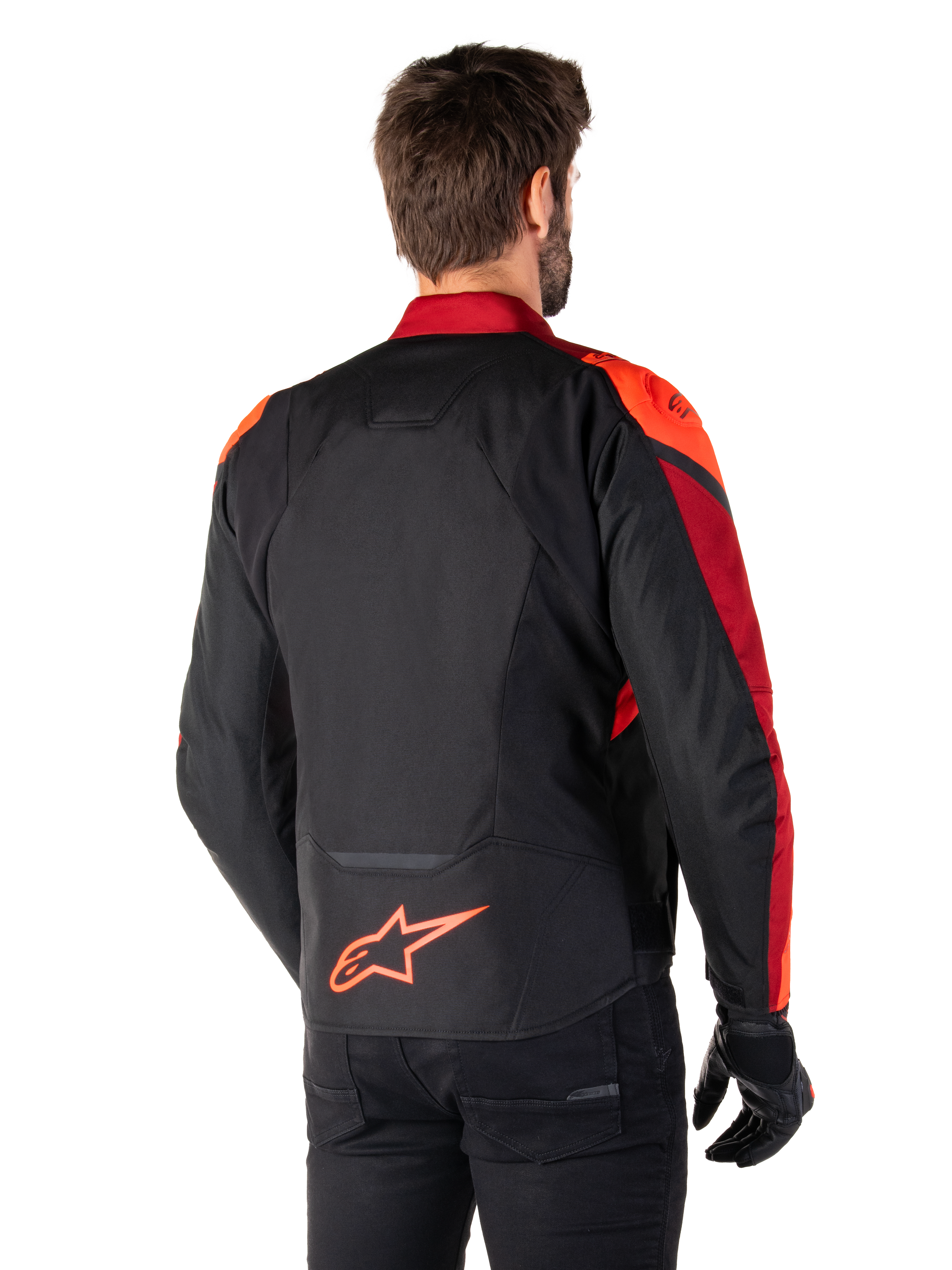 Rear view of a man wearing the Alpinestars T-Jaws V4 Waterproof Jacket in Black Red Fluo Dark Red, featuring vibrant red accents on the shoulders and sleeves, a fluo red Alpinestars logo on the lower back, paired with black pants and gloves.