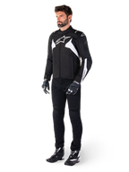 Male model wearing Alpinestars T-Jaws V4 Waterproof Jacket in Black and White, sport textile jacket featuring a white star logo and sleeve accents, styled with black motorcycle pants, gloves, and boots for a complete road riding look.