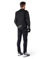 Alpinestars T-Jaws V4 Waterproof Jacket, Black and White, rear view showing white star logo on lower back, worn by model with black riding pants, black gloves, and white and black motorcycle boots.