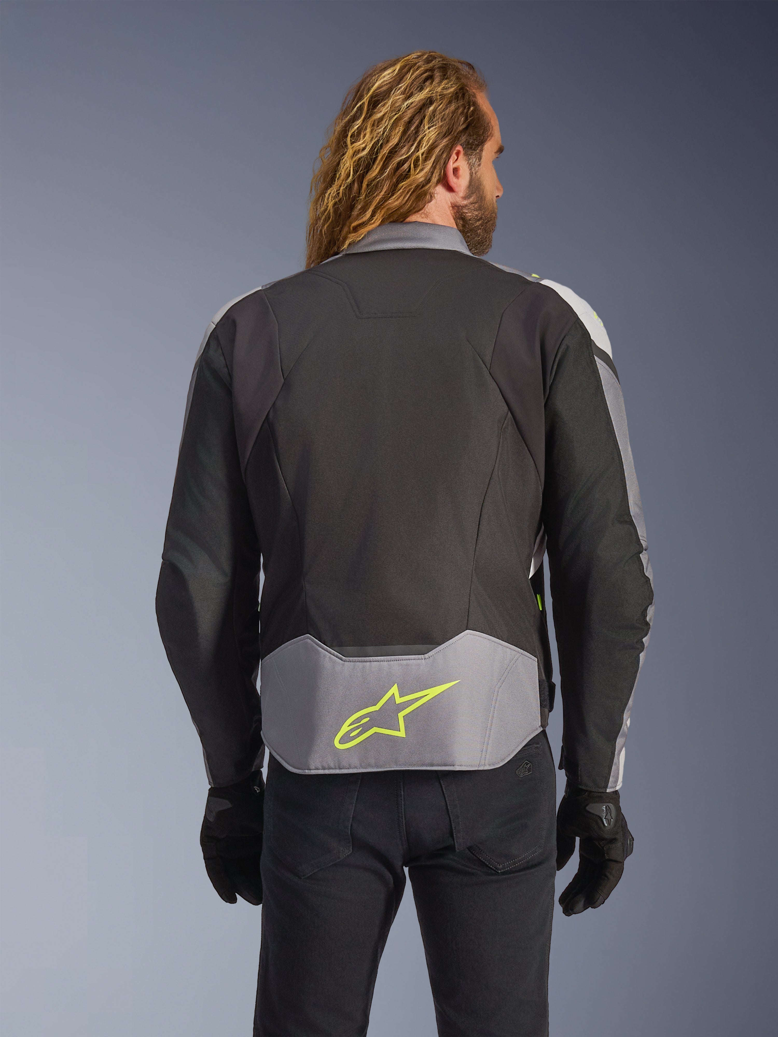 Alpinestars T-Jaws V4 Waterproof Jacket, Black Ice Gray Dark Gray, rear view on model, featuring a light gray lower back panel with a prominent neon yellow star logo, multi-panel textile construction, and a sporty silhouette, worn with black gloves and dark pants.