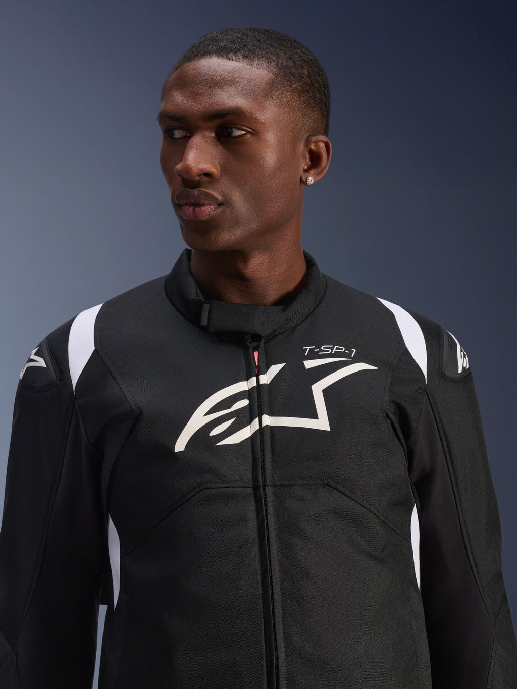 Alpinestars T-SP 1 V2 Waterproof Jacket worn by a model, black and white textile motorcycle jacket, large white Alpinestars logo and T-SP-1 branding on the chest, sporty design with protective shoulder sliders