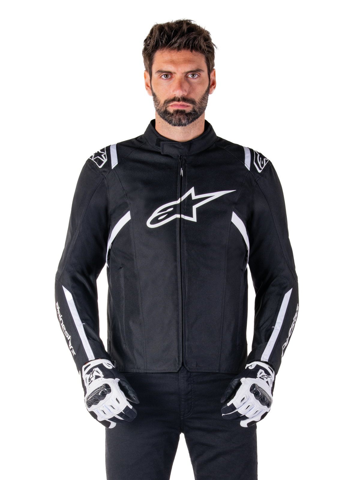 Alpinestars T-SPS V2 Waterproof Jacket i svart och vitt, vy framifrån på modell, vattentät textiljacka för motorcykel med vita ränder på axlar och ärmar, stor vit Alpinestars-logotyp på bröstet, bärs med skyddande motorcykelhandskar, stilren sportinspirerad siluett