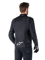 Alpinestars T-SPS V2 Waterproof Jacket, Black and White, rear view of a male rider wearing the jacket, white Alpinestars logo on the lower back, sport cut textile construction, worn with black riding pants and gloves