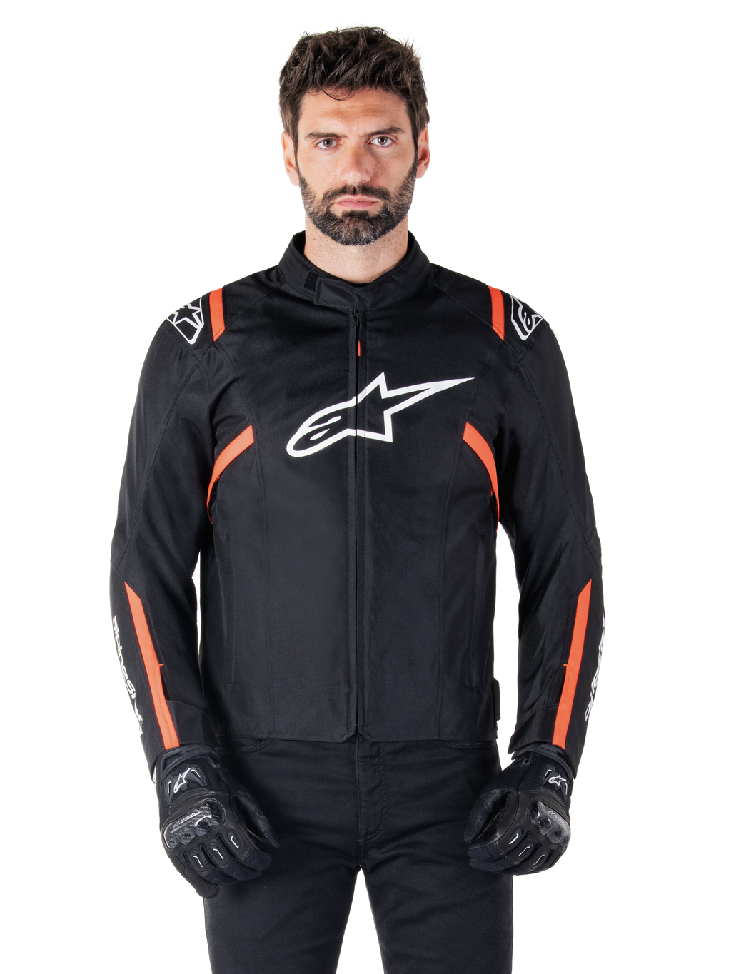 Alpinestars T-SPS V2 Waterproof-jacka, svart, vit och röd fluo, bärs av en manlig modell med svarta mc-handskar, med en stor vit Alpinestars-logotyp på bröstet och livfulla orangea detaljer på axlar och ärmar.