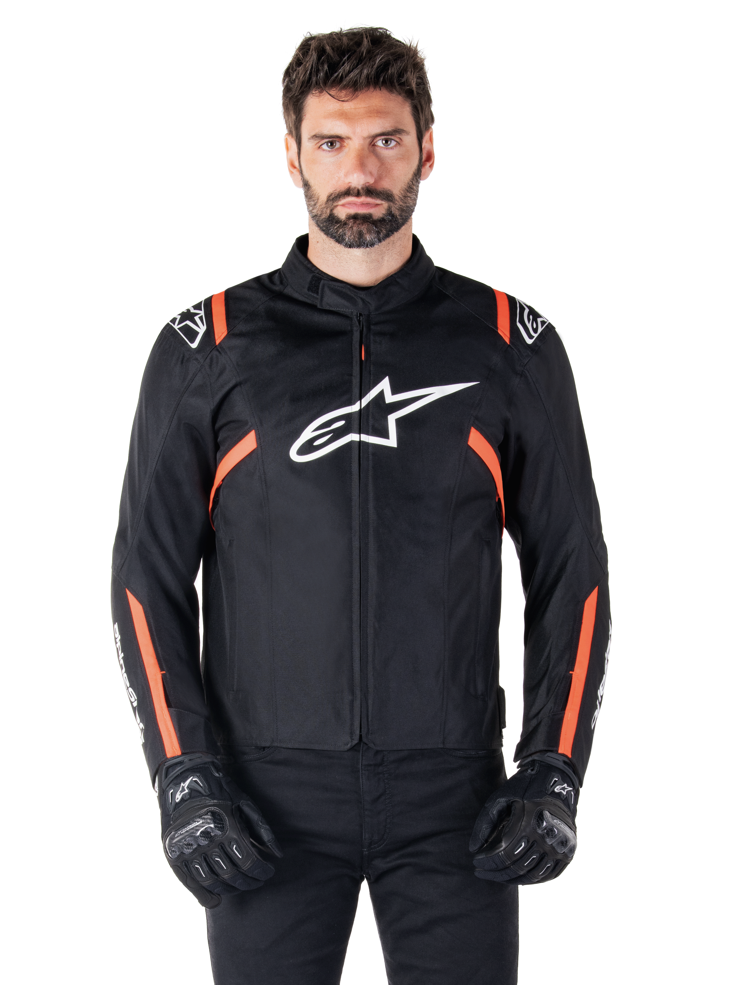 Alpinestars T-SPS V2 Waterproof-jacka, svart, vit och röd fluo, bärs av en manlig modell med svarta mc-handskar, med en stor vit Alpinestars-logotyp på bröstet och livfulla orangea detaljer på axlar och ärmar.