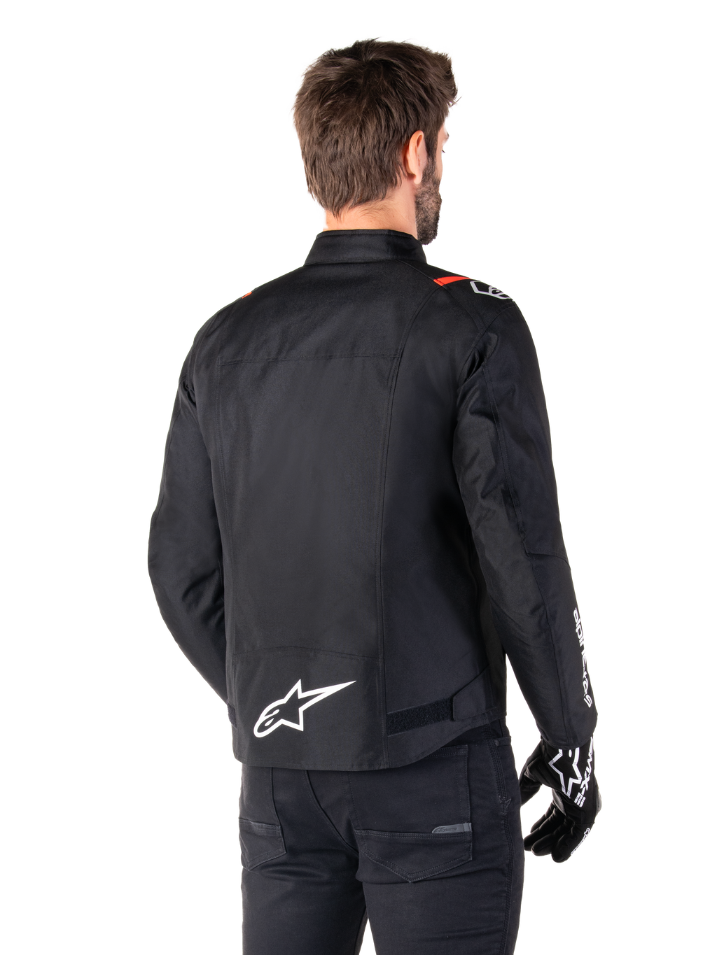Alpinestars T-SPS V2 Waterproof-jacka, Black White Red Fluo, sedd bakifrån, med vit Alpinestars-logotyp på nedre delen av ryggen och röda detaljer på axlarna, bärs med svarta körhandskar och byxor, sportig textiljacka för motorcykel.