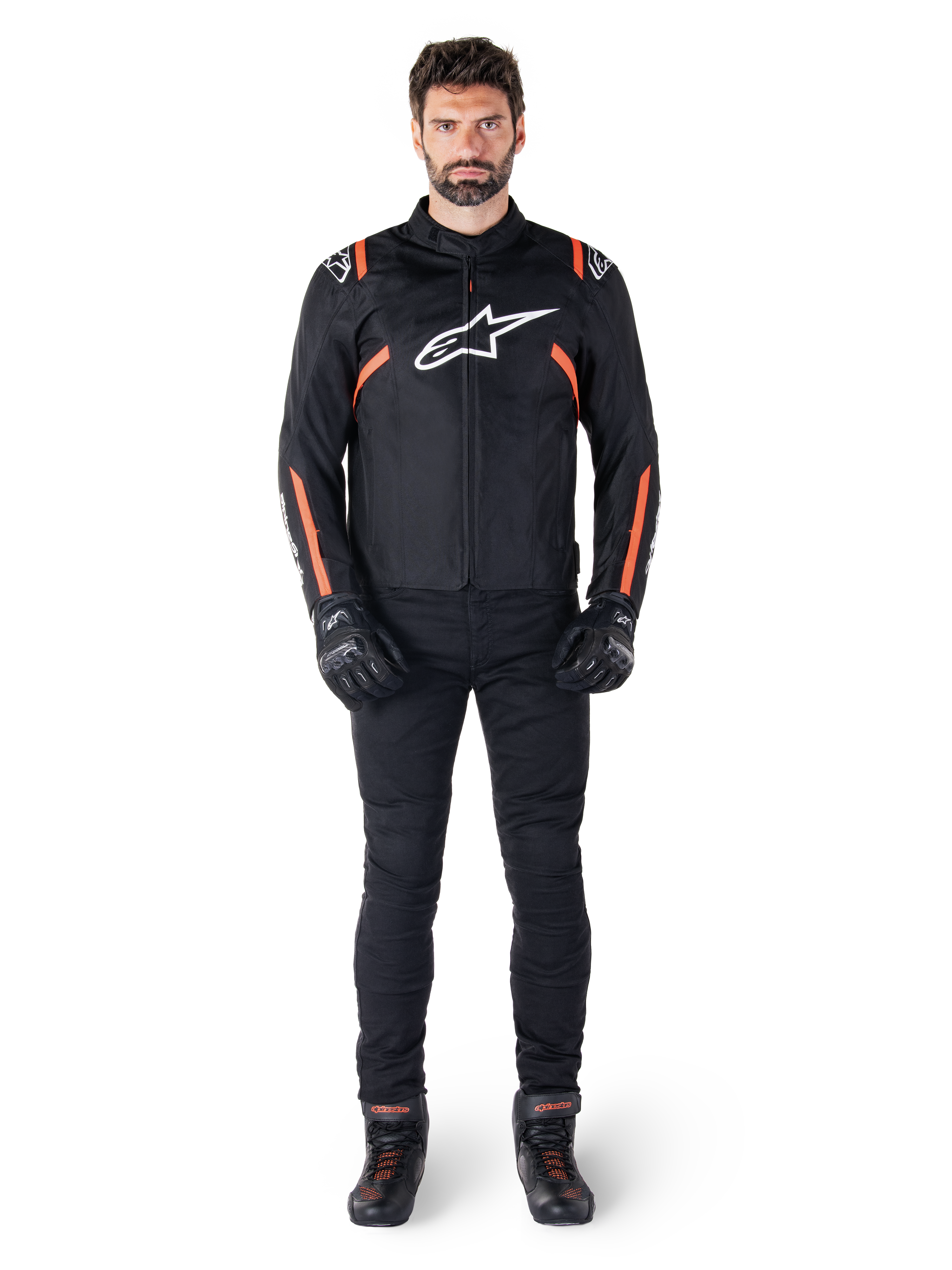 Manlig modell som bär Alpinestars T-SPS V2 Waterproof-jacka i Black White Red Fluo, kombinerad med svarta motorcykelbyxor och handskar, med en vit Alpinestars-logotyp på bröstet och röda detaljer på ärmarna.