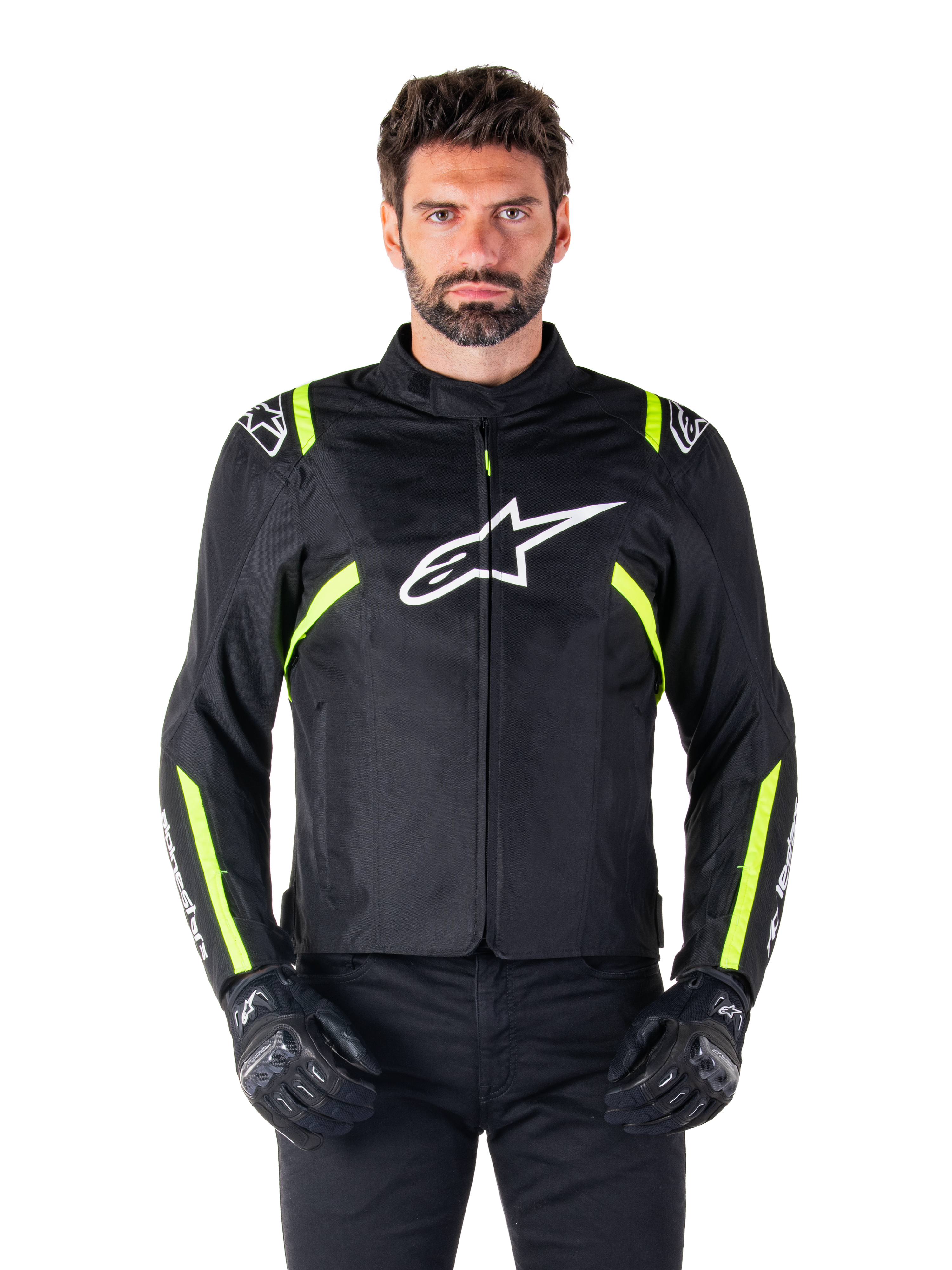 Alpinestars T-SPS V2 Waterproof Jacket, motorcykeljacka, svart med vita och neongula detaljer, bärs av en modell med svarta handskar, vit stjärnlogotyp på bröstet och neongula ränder på ärmar och axlar, sportig textilutrustning för körning i alla väder