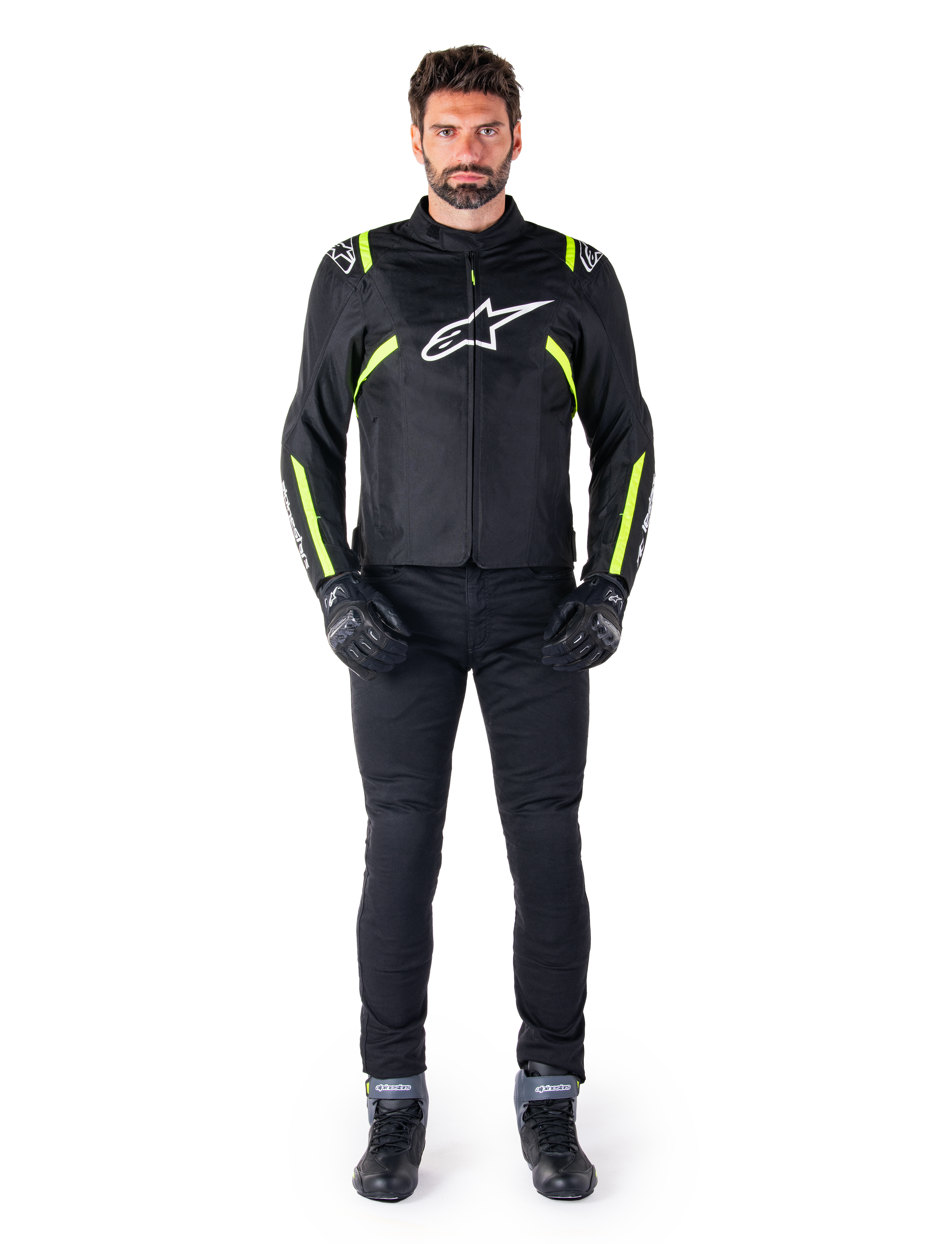 Alpinestars T-SPS V2 Vattentät Jacka, svart, vit och gul fluo, bärs av en modell med svarta körbyxor och handskar, vit Alpinestars-logotyp på bröstet och fluorescerande detaljer på axlar och ärmar, sportig motorcykelutrustning