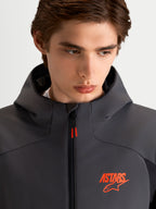 Alpinestars Aeroshell WP jacka, vattentät motorcykeljacka i softshell, svart och mörkgrå med huva och orange ASTARS-logotyp, närbild på modell