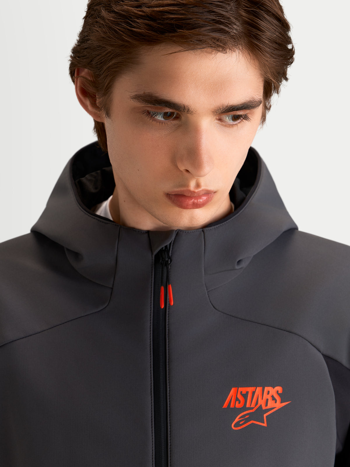 Alpinestars Aeroshell WP jacka, vattentät motorcykeljacka i softshell, svart och mörkgrå med huva och orange ASTARS-logotyp, närbild på modell