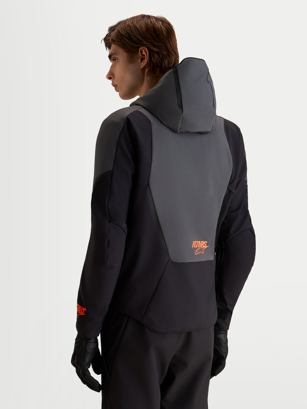 Alpinestars Aeroshell WP jacka, vattentät motorcykeljacka i softshell, svart och mörkgrå med integrerad huva och detaljer på ryggpanelen, vy bakifrån på manlig förare