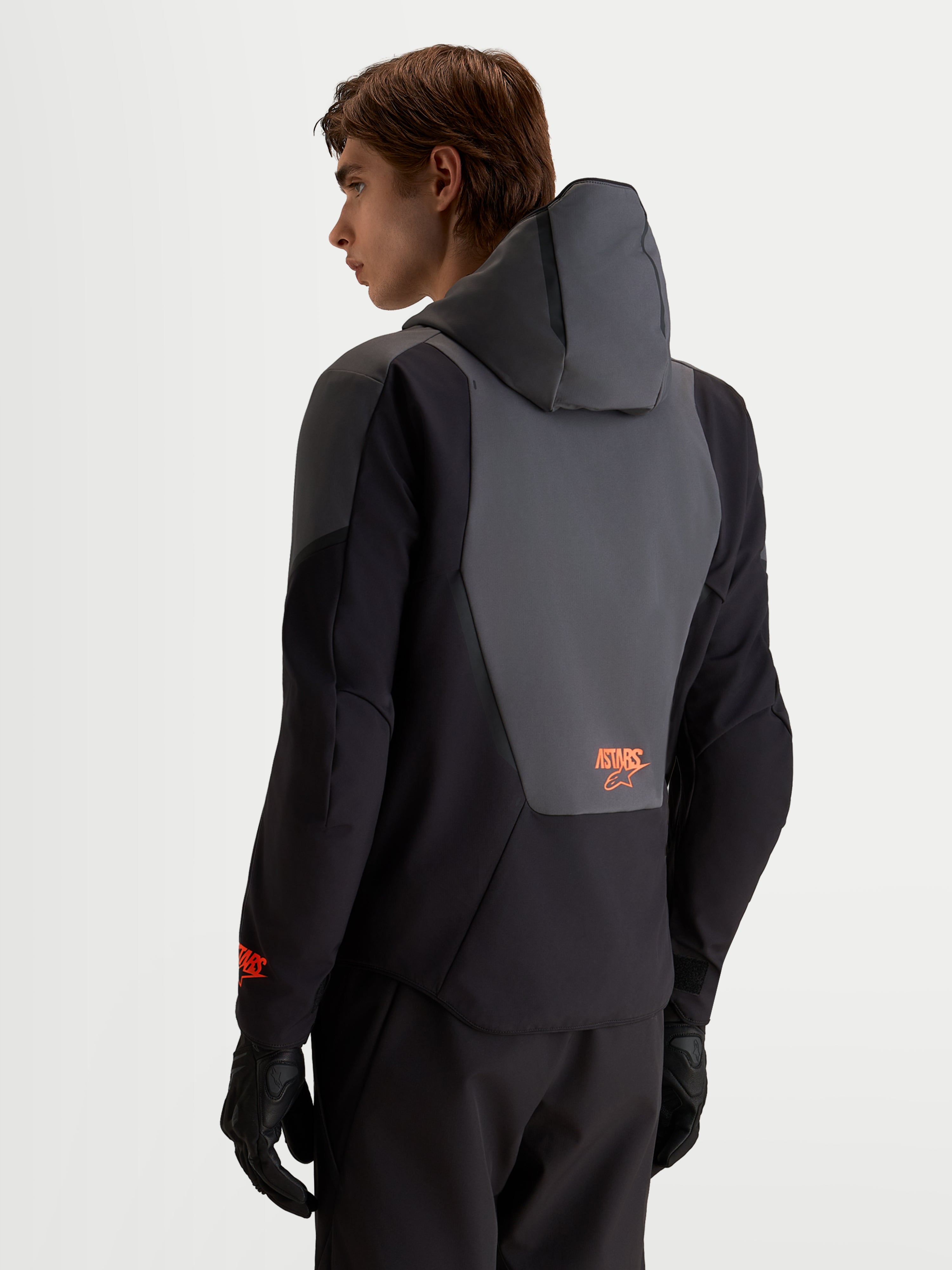 Alpinestars Aeroshell WP jacka, vattentät motorcykeljacka i softshell, svart och mörkgrå med integrerad huva och detaljer på ryggpanelen, vy bakifrån på manlig förare