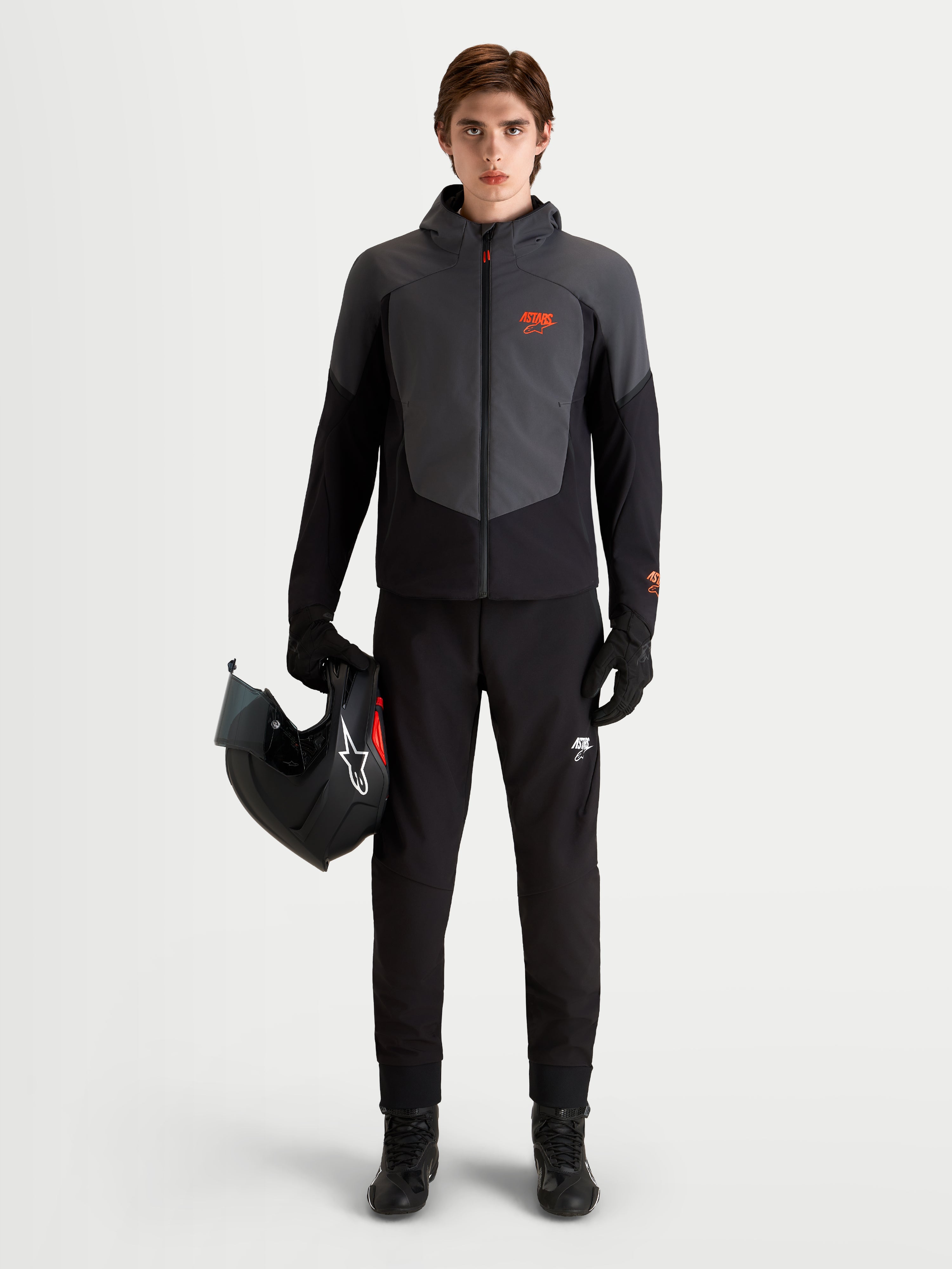 Alpinestars Aeroshell Wp jacka, vattentät motorcykeljacka för herr i svart och mörkgrå, med huva och CE-certifierat skydd, bärs av en modell som håller en motorcykelhjälm