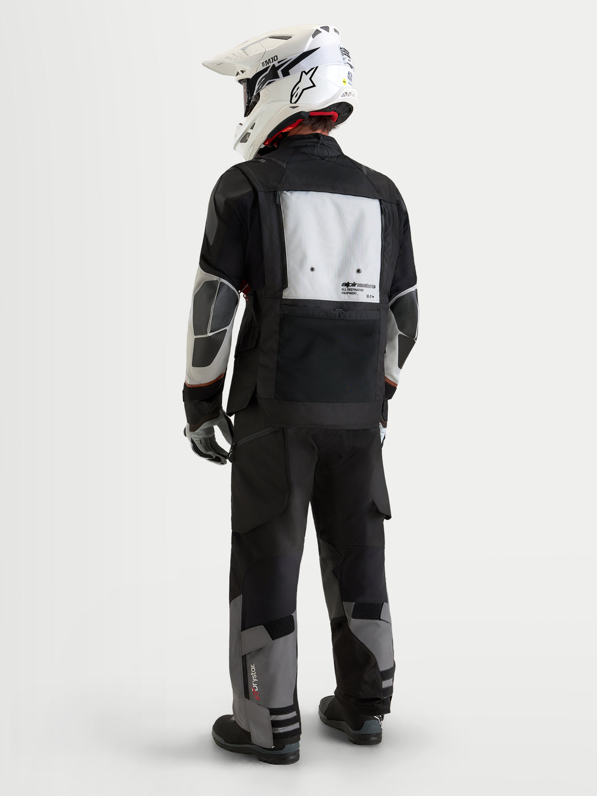 Alpinestars Harok V2 Drystar jacka, äventyrs-MC-jacka för herr, mörkgrå, isgrå och svart, vy bakifrån som visar modulär ventilationspanel och matchande äventyrsbyxor med en vit off-road-hjälm