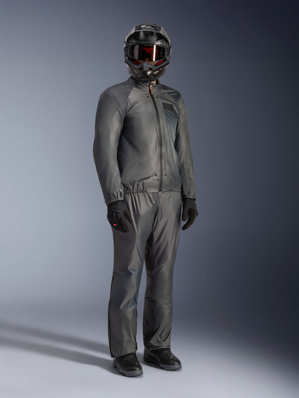 Förare som bär Alpinestars Borrego Drystar®-jacka i Warm Gray, komplett äventyrsutrustning med matchande grå byxor, svart helhjälm med goggles och svarta handskar, med en stilren vattentät textildesign.