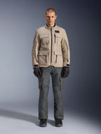Alpinestars Borrego Drystar®-jacka, äventyrsmotorcykeljacka, Warm Gray, bärs av en modell med mörkgrå körbyxor och svarta handskar, med flera cargo-fickor och en slitstark textilkonstruktion med en klassisk vaxad canvas-look.