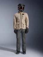 Alpinestars Borrego Drystar®-jacka i Warm Gray, äventyrsmotorcykeljacka med fyra cargo-fickor framtill, kombinerad med mörkgrå mc-byxor, svart offroad-hjälm och svarta handskar, med en robust vaxad canvas-look