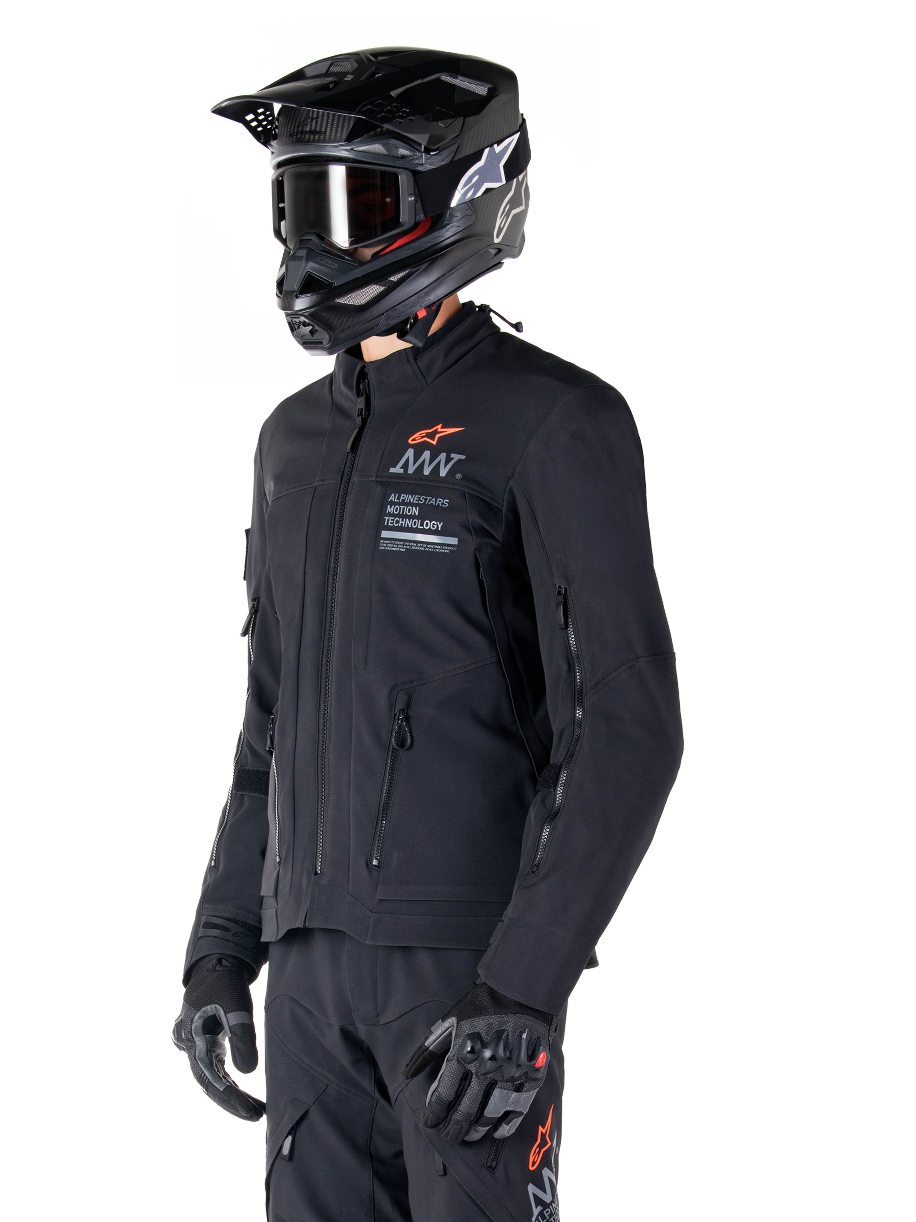 Alpinestars AMT-8 Stretch Drystar® XF Jacka, svart, bärs av en förare med matchande äventyrsbyxor och handskar, svart motocrosshjälm och goggles, ventilationsöppningar med dragkedja på bröstet och armarna, Alpinestars Motion Technology-branding med en orange logotyp, premium adventure-touringutrustning
